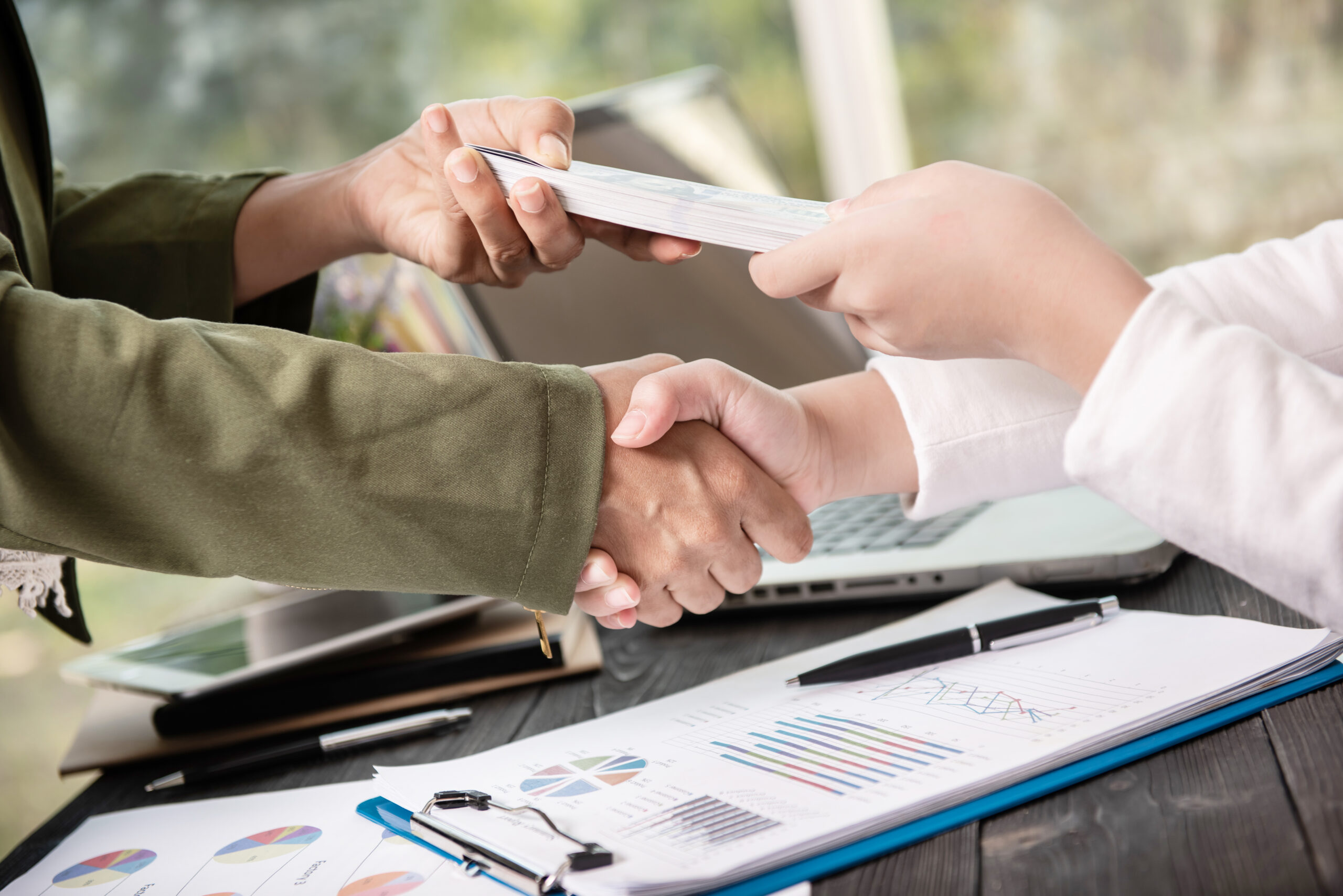 Business people shaking hands, finishing up meeting. businessman giving money to his partner while making contract - bribery and corruption concepts.